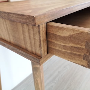 May include: A wooden side table with a single drawer that is open. The table has a light brown stain and four legs.