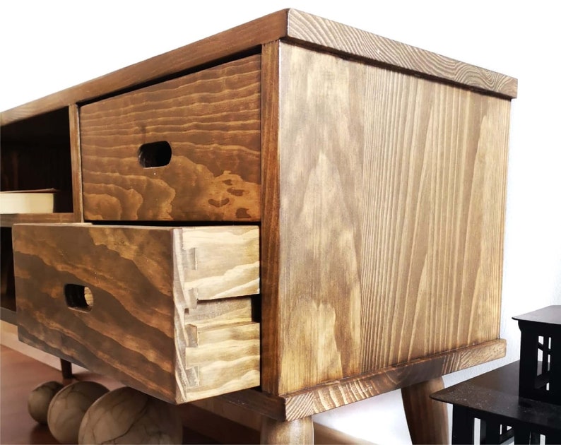 May include: A wooden entertainment center with a dark brown stain. The cabinet has three drawers and a shelf. The drawers have a simple, rectangular design with a small, rectangular cutout for a handle. The cabinet has a simple, rectangular design with rounded edges. The cabinet is sitting on four legs.