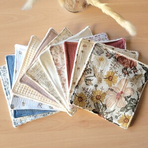 Puede incluir: Un conjunto de 12 discos de algodón reutilizables en varios patrones florales, incluyendo un rosa claro, un azul claro y un verde claro. Los discos están dispuestos en forma de abanico, con los patrones florales mirando hacia afuera.