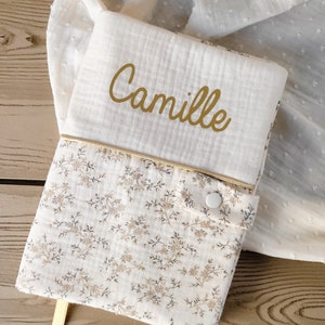 Può includere: Una copertina per libro per bambini bianca con un motivo floreale e il nome "Camille" in oro. Presenta un bordo dorato, una chiusura con bottone e un segnalibro a nastro dorato. Il tessuto è morbido.