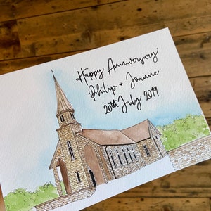 May include: A watercolor painting of a church with a tall steeple. The painting is on a white card with the text "Happy Anniversary Philip & Joanne 20th July 2019" written in black ink.