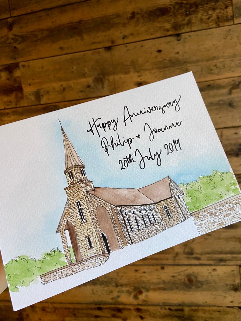 May include: A watercolor painting of a church with a tall steeple. The painting is on a white card with the text "Happy Anniversary Philip & Joanne 20th July 2019" written in black ink.