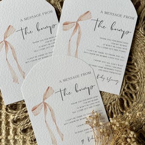 May include: Three white cards with a watercolor illustration of a pink bow. The cards have the text "A message from the bump" and a message from the baby to the guests.