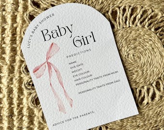 May include: A white card with a pink bow illustration and the text "Lucy's Baby Shower Baby Girl Predictions Name: Due Date: Weight: Eye Colour: Hair Colour: Personality Traits from Mum: Personality Traits from Dad: Advice for the Parents:"