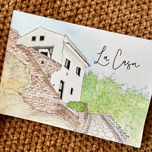 May include: A watercolor painting of a white house with a brick wall and a stone path leading up to it. The house has a few windows and a small balcony. The painting is titled "La Casa" in cursive.