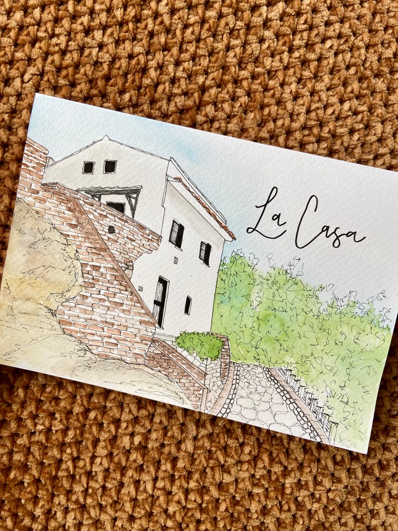 May include: A watercolor painting of a white house with a brick wall and a stone path leading up to it. The house has a few windows and a small balcony. The painting is titled "La Casa" in cursive.