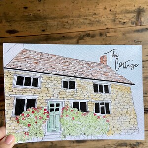 May include: Watercolor illustration of a stone cottage with a green door and red flowers. The text "The Cottage" is written in cursive above the house.