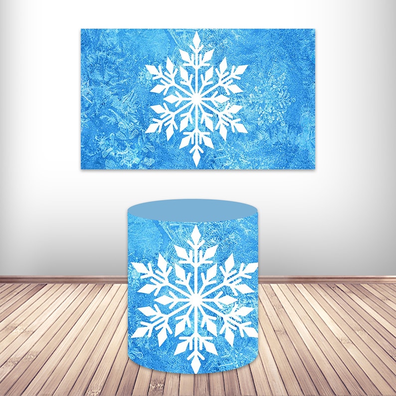 May include: A blue cylinder with a white snowflake design. The cylinder is sitting on a wooden floor. The background is a white wall with a blue rectangle with a white snowflake design.