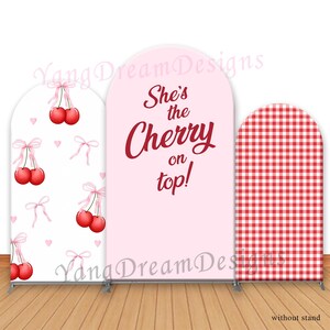 May include: Three backdrop panels for a party. The center panel is pink with the text "She's the Cherry on top!" in red. The left panel is white with a repeating pattern of red cherries with pink bows. The right panel is red and white gingham.