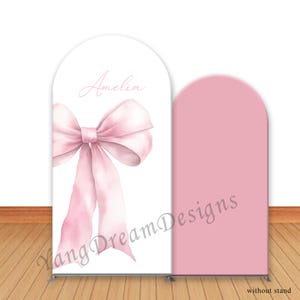 May include: A white arch-shaped backdrop with a watercolor-style pink bow and the name "Amelia" in cursive. A solid pink arch-shaped backdrop is next to it. The text "Yang Dream Designs" is at the bottom of the white backdrop.