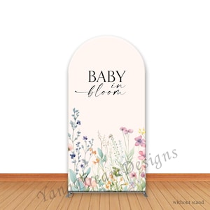 May include: An arched backdrop cover featuring a pale cream background with a watercolour floral print at the base in shades of blue, pink, and green. The text BABY in bloom is printed in black in the centre of the upper portion of the arch.