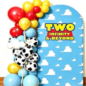 May include: A blue arched backdrop featuring a white cloud pattern and the text TWO INFINITY & BEYOND in yellow and red. Beside it is a balloon garland with red, yellow, and light blue balloons, plus white balloons with black cow print spots.
