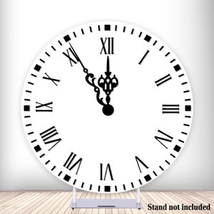 Peut inclure: Une toile de fond ronde blanche en forme d'horloge avec des chiffres romains noirs et des aiguilles. Le cadran de l'horloge est réglé sur 12h00. La toile de fond est sur un sol en bois avec un support argenté. "Stand not included" est écrit en noir en bas de l'image.