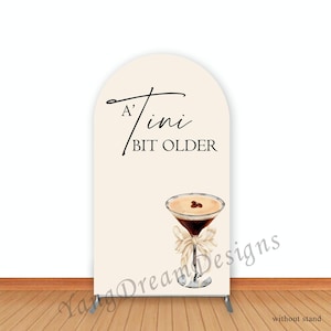 May include: A white arch backdrop with the text "A'tini Bit Older" and a watercolor illustration of a martini glass with coffee beans on top.