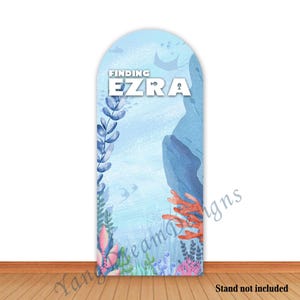 Può includere: Uno sfondo blu e bianco con il testo "Finding Ezra" in bianco. Lo sfondo presenta un'illustrazione ad acquerello di coralli, alghe e pesci.