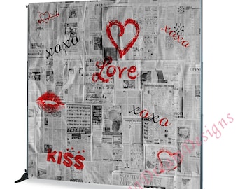 May include: A backdrop featuring a collage of newspaper clippings with red accents. The words "Love," "Kiss," and "xoxo" are written across the surface, along with a heart and lips graphic. The backdrop is supported by a black stand.