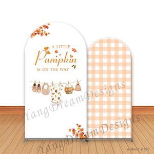 May include: A white backdrop with an arch shape, featuring the text "A Little Pumpkin Is On The Way." The design includes illustrations of baby clothes, shoes, and a hat hanging on a clothesline, with fall leaves. A second backdrop with an arch shape has a peach and white gingham pattern.