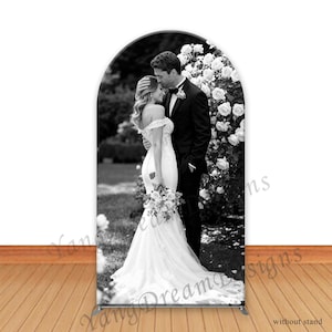 Peut inclure: Toile de fond de mariage en noir et blanc avec un couple s'embrassant devant une arche de roses. La mariée porte une robe blanche à épaules dénudées, et le marié un smoking noir. Le texte "Xang Dream Designs" et "without stand" est imprimé.