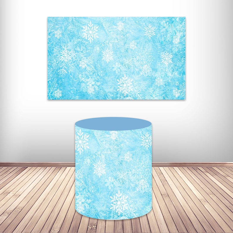 May include: A light blue cylinder with a white snowflake pattern. The cylinder is sitting on a wooden floor. There is a light blue rectangle with a white snowflake pattern behind the cylinder.