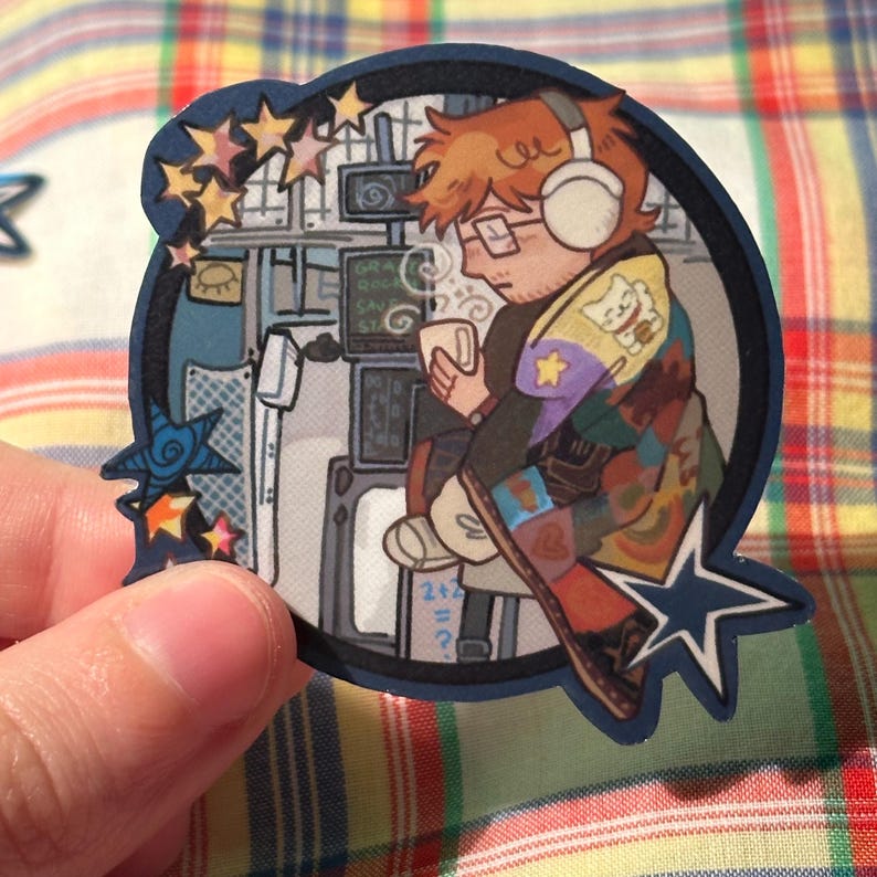 May include: A die-cut sticker featuring an illustration of a person wearing headphones, glasses, and a colorful patchwork jacket, holding a mug. The background includes screens and stars. The sticker is held by a hand.