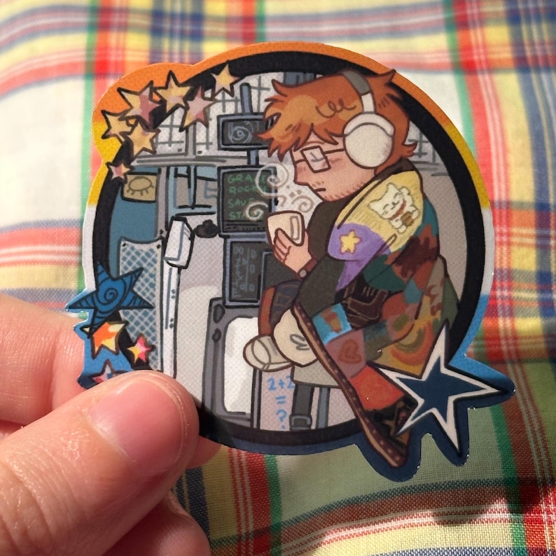 May include: A colorful sticker featuring a person with headphones, glasses, and a beard, holding a mug. The person is surrounded by computer screens and stars. The sticker has a rainbow border and the text "GRA ROCK SAV ST".