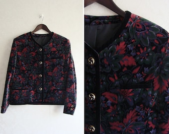 May include: A black velvet jacket with a floral pattern in shades of red, green, and blue. The jacket has a round neckline, long sleeves, and a button closure.