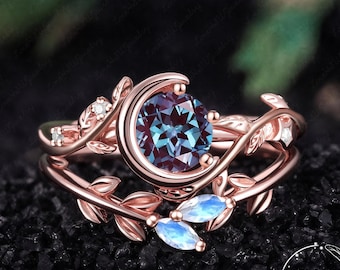 May include: A rose gold ring featuring a round, color-changing center stone cradled by a crescent moon shape. The band is designed with intricate leaf motifs and small accent stones, including two marquise-cut iridescent gems. Text reads LOVE HSW JEWELRY ART.