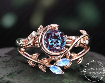 May include: A rose gold ring with a crescent moon design and a blue gemstone. The ring is set with smaller gemstones and has a leafy design.