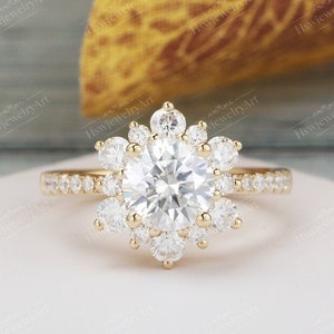 May include: A gold engagement ring with a large round center stone surrounded by a halo of smaller round stones. The ring has a delicate band with smaller stones set along the sides.
