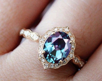 May include: A gold ring with a large oval-shaped blue gemstone surrounded by a halo of smaller diamonds. The ring is set on a finger.