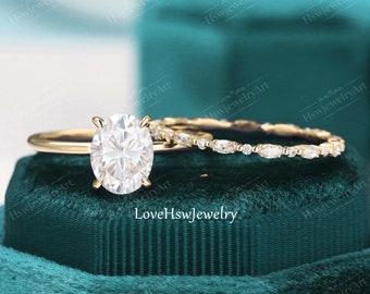 May include: A gold engagement ring set with a large oval-shaped diamond and a matching band with smaller diamonds. The ring is displayed in a green velvet ring box.
