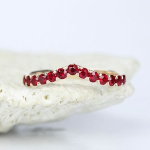 Könnte beinhalten: Ein Goldring mit einer geschwungenen Reihe roter Rubin-Steine.