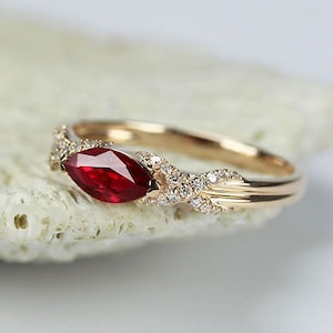 Puede incluir: Un anillo de oro con un rubí rojo en forma de marquesa y una banda de pequeños diamantes.