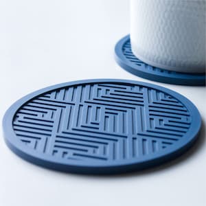May include: A set of two blue silicone coasters with a geometric pattern. The coasters are round and have a raised edge.
