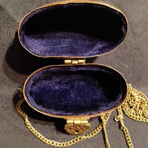 Op de afbeelding: Een gouden ovale handtas met een blauw fluwelen interieur en een gouden kettingband.