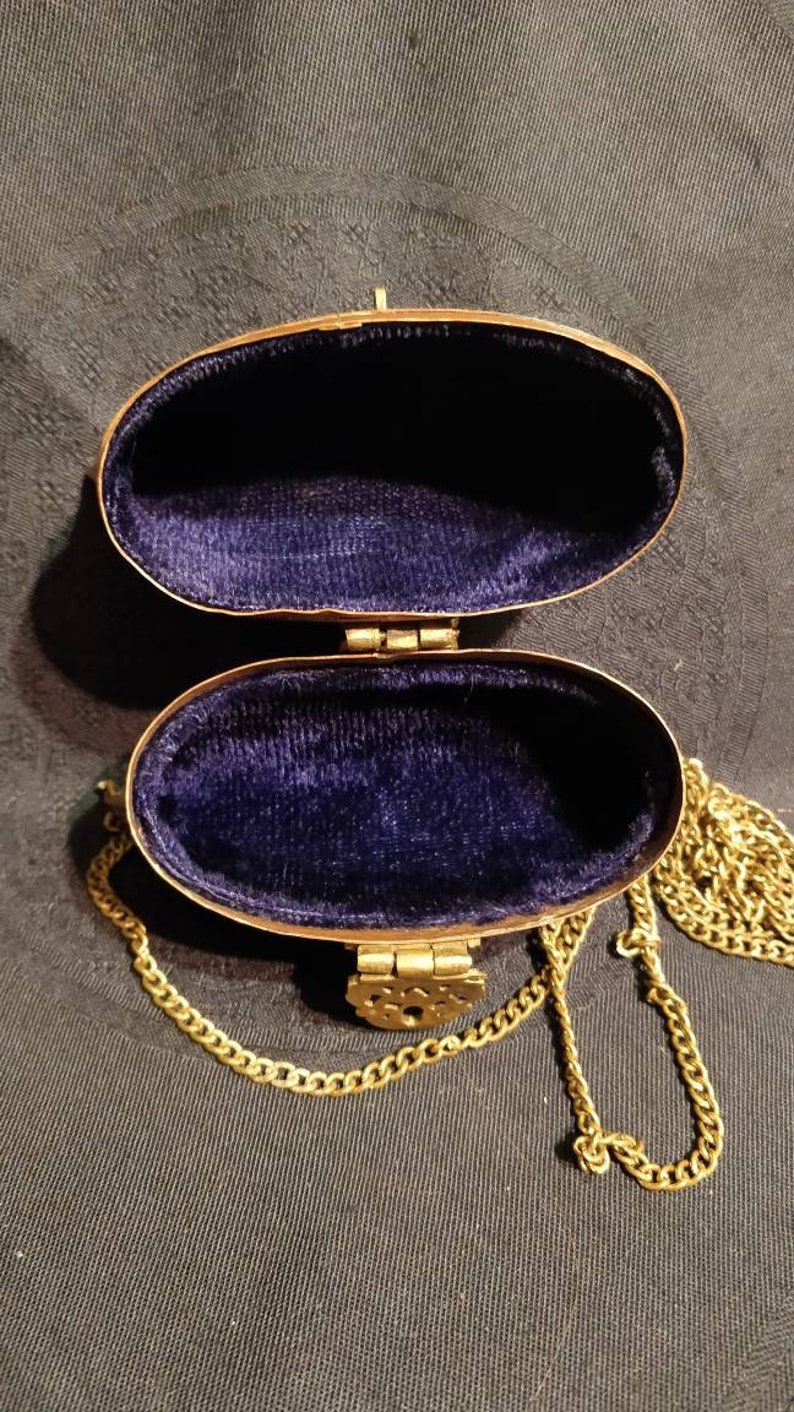 Op de afbeelding: Een gouden ovale handtas met een blauw fluwelen interieur en een gouden kettingband.