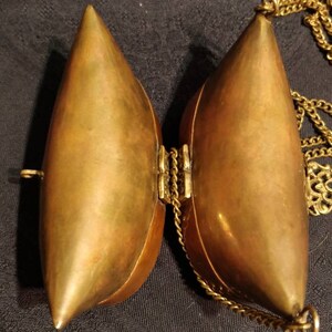 Op de afbeelding: Een messing scharnierende tas met een ketting eraan. De tas is open en de binnenkant is zichtbaar. De tas is traanvormig.