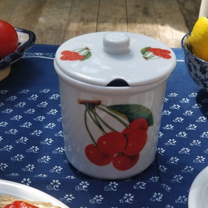 Peut inclure: Pot en céramique blanche avec un couvercle, orné d'un motif de cerises. Le pot présente un motif de cerises rouges avec des feuilles et des tiges vertes. Le couvercle a un petit bouton et un motif de cerises sur le dessus.