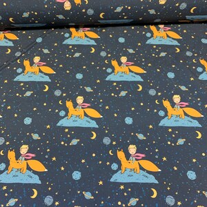Könnte beinhalten: Ein dunkelblauer Stoff mit einem sich wiederholenden Muster eines kleinen Prinzen, der einen Fuchs auf einem zunehmenden Mond reitet. Der Hintergrund ist mit kleinen Sternen und Planeten gefüllt.