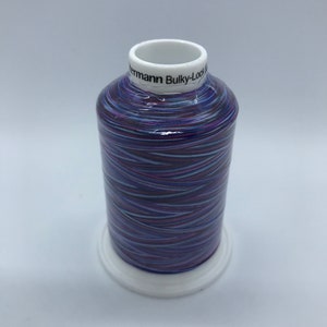 Könnte beinhalten: Eine Spule mit violettem, weißem und schwarzem Stickgarn mit dem Text "Sulky-Lock Bulky" auf dem Etikett.