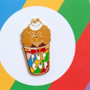 Puede incluir: Pin de esmalte dorado con un caniche marrón que lleva un sombrero blanco y una pajarita roja, dentro de una taza colorida con el texto "Pup Cup".