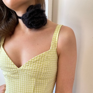 May include: A green and white gingham sleeveless top with a sweetheart neckline. The top is fitted and has a boned bodice.