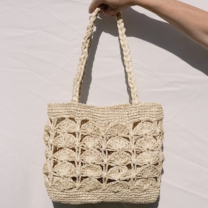 May include: A cream-colored crocheted tote bag with a woven handle. The bag has a delicate, openwork design with a pattern of small circles.