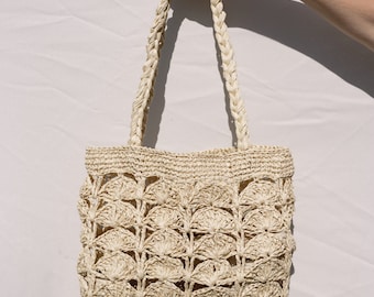 May include: A cream-colored crocheted tote bag with a woven handle. The bag has a delicate, openwork design with a pattern of small circles.