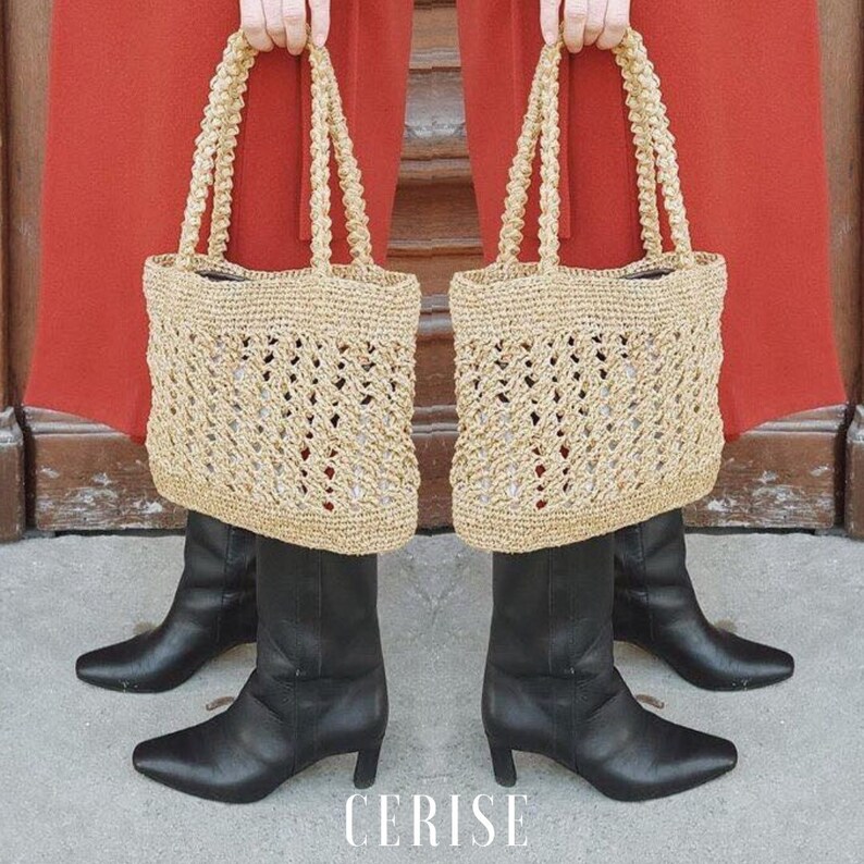 May include: A pair of beige crochet tote bags with thick rope handles. The bags are hanging from the hands of a person wearing a red skirt and black boots. The word "CERISE" is printed in white on the ground.