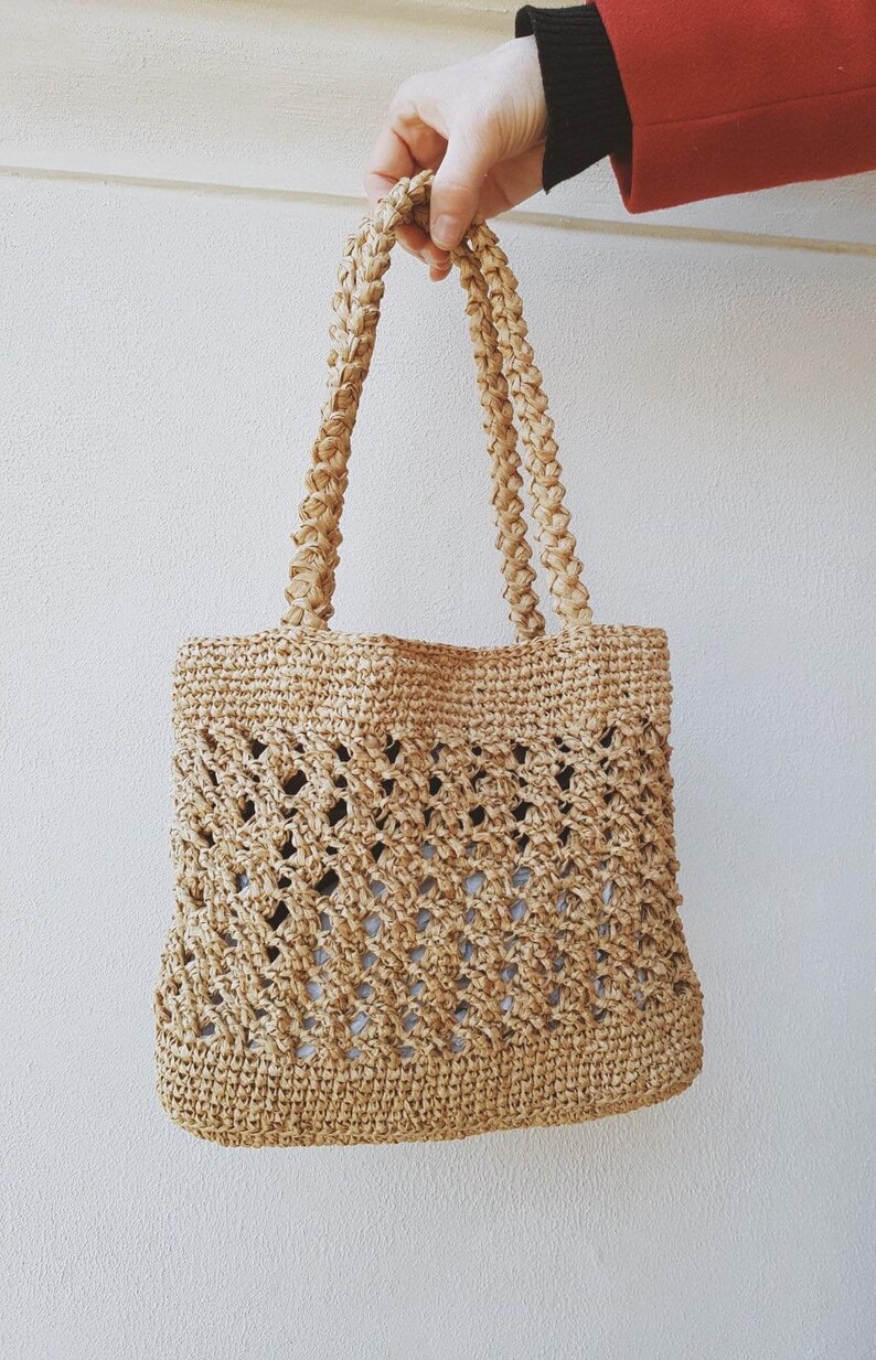 May include: A woven straw tote bag with a crocheted design. The bag has two thick, braided straps.