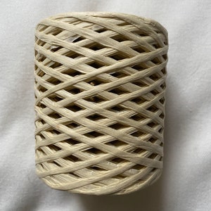 May include: A spool of natural-coloured paper twine, wound in a criss-cross pattern. The twine is made of thin, woven strips of paper.