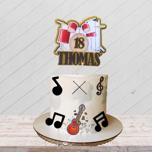 May include: A white cake with a drum set topper that says "18 Thomas". The cake is decorated with musical notes and a guitar.