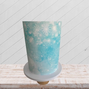 Könnte beinhalten: Ein blauer und weißer Kuchen, der mit Schneeflocken und Sternen verziert ist. Der Kuchen steht auf einem weißen Kuchenständer.