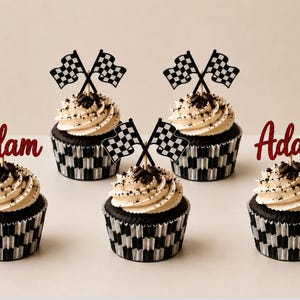 Op de afbeelding: Vijf cupcakes met een donkere chocoladebasis en witte frosting, afgewerkt met donkere hagelslag. Twee cupcakes hebben de naam Adam in rode glittercursief, terwijl drie cupcakes zijn voorzien van gekruiste zwart-witte racevlaggetjes.
